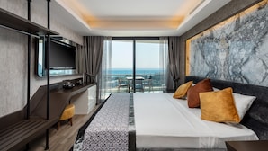 A modern hotel room with a large bed, a desk, a flat-screen TV, and a balcony with a view of the sea. - Elite Luxury Suite & Spa (Alanya)
