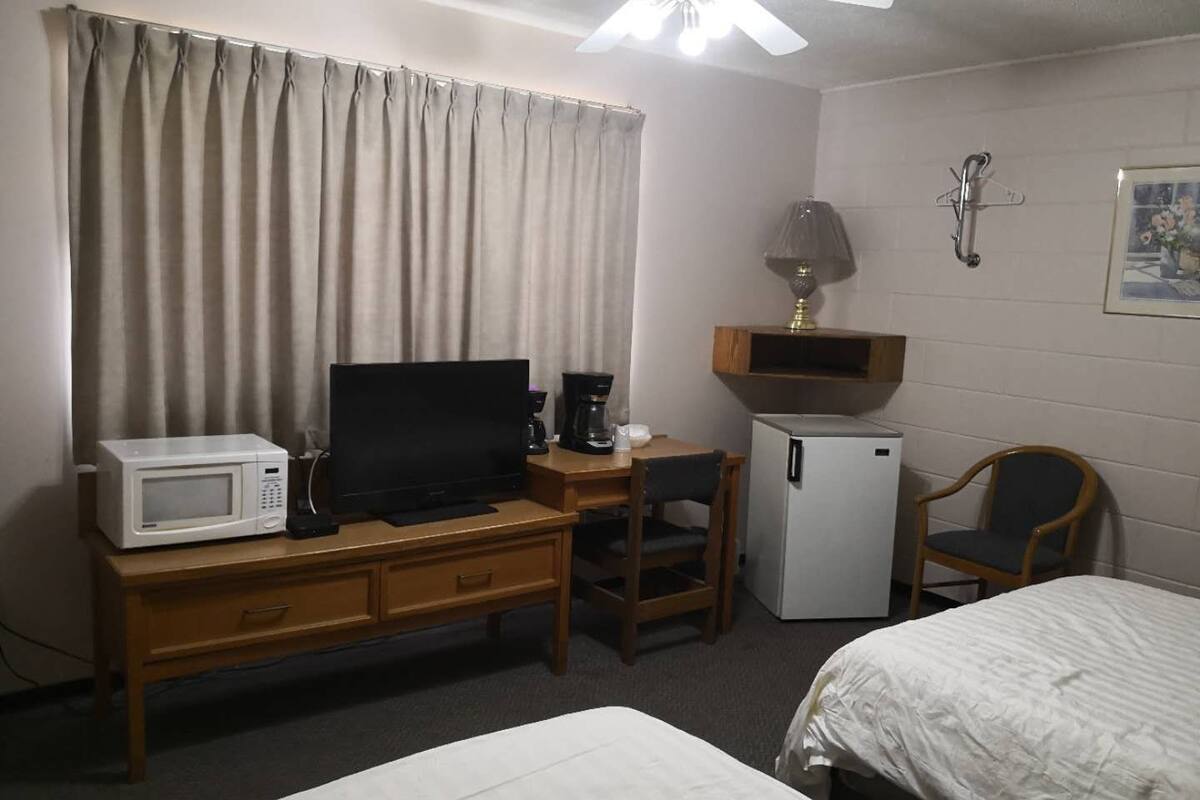 Habitación de hotel con cama, escritorio con computadora, microondas, cafetera, refrigerador, silla y ventilador de techo.