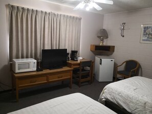 A hotel room with a bed, a desk with a computer, a microwave, a coffee maker, a refrigerator, a chair, and a ceiling fan.