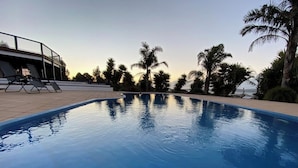 A swimming pool with a clear view of the surrounding palm trees and a building with a balcony in the background.