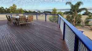 A wooden deck with a table and chairs, overlooking a beach and ocean.