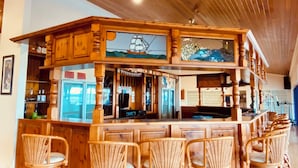 A wooden bar area with a high ceiling, wicker chairs, and a ship-themed stained glass window.