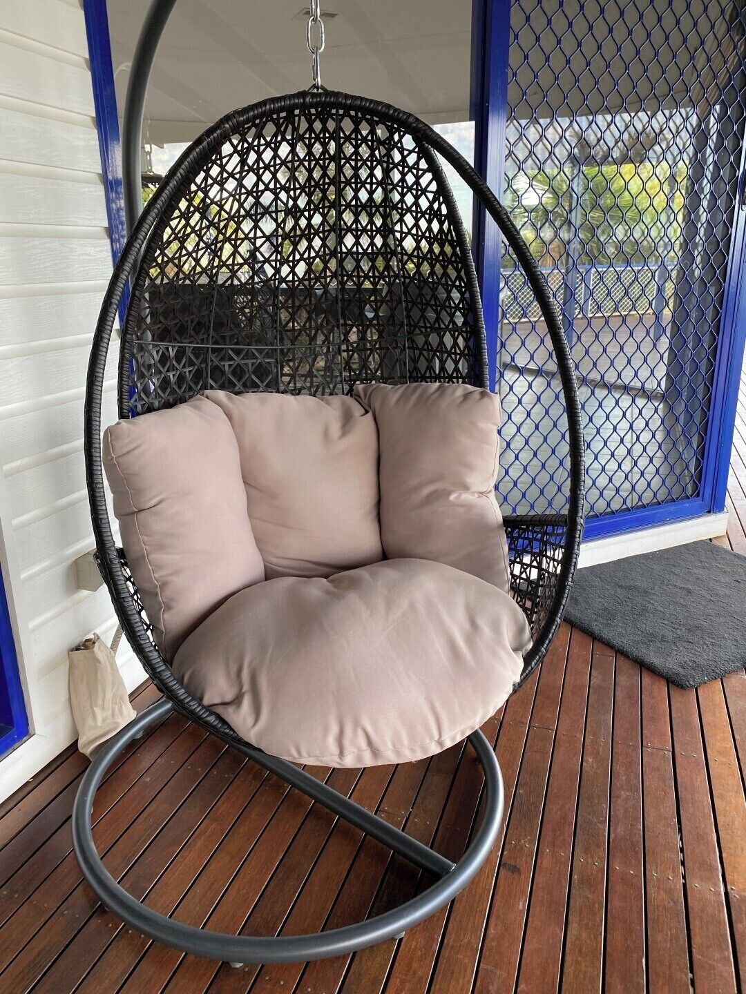 A black wicker swing chair with beige cushions on a wooden deck.