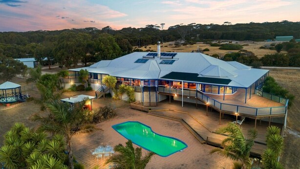 A large, modern building with multiple levels, a swimming pool, and surrounding greenery.