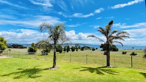 A grassy field with two palm trees and a fence, with a body of water and distant hills in the background.