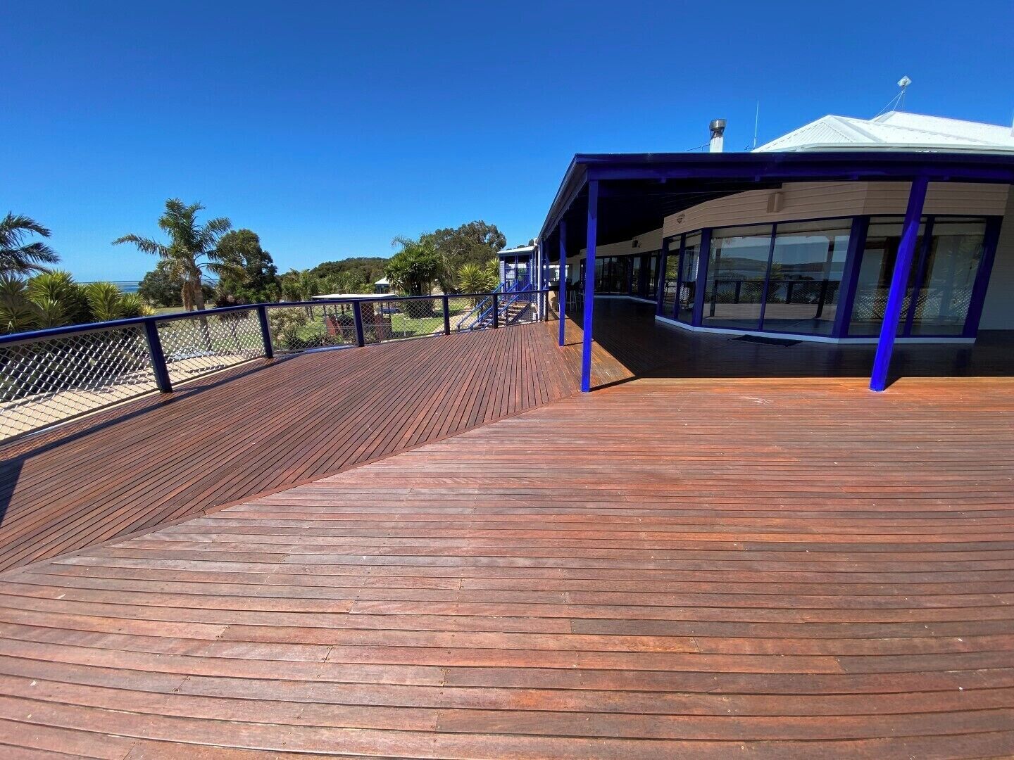 A wooden deck with a blue railing, leading to a building with large windows and a covered area.