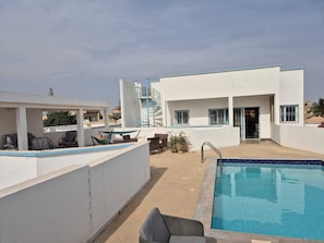 A rooftop pool area with a pool, lounge chairs, and a building with a blue railing.