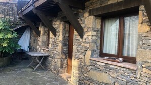 A stone building with a wooden balcony, a window with curtains, and a small table outside. - Rural apartment L'Alzina for 4 people (Tavertet)