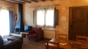 A cozy living room with a fireplace, a television, and a dining area with wooden furniture. - Rural apartment L'Alzina for 4 people (Tavertet)
