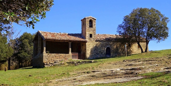 Un bâtiment en pierre doté d’un clocher, d’un porche couvert et, au fond, d’une colline verdoyante.