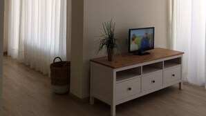 A living room with a wooden TV stand, a potted plant, and a wicker basket. - Beautiful apartment by the sea with pool (Roquetas de Mar)