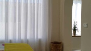 A room with a bed, a bench, a window with curtains, and a plant. - Beautiful apartment by the sea with pool (Roquetas de Mar)