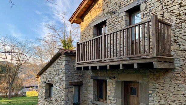 A stone building with a wooden balcony, a door, and windows.