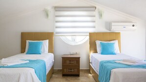 Une chambre d’hôtel avec deux lits, une petite table de chevet en bois, une fenêtre avec des stores et un appareil de climatisation.