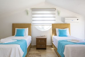 A hotel room with two beds, a small wooden nightstand, a window with blinds, and an air conditioning unit.