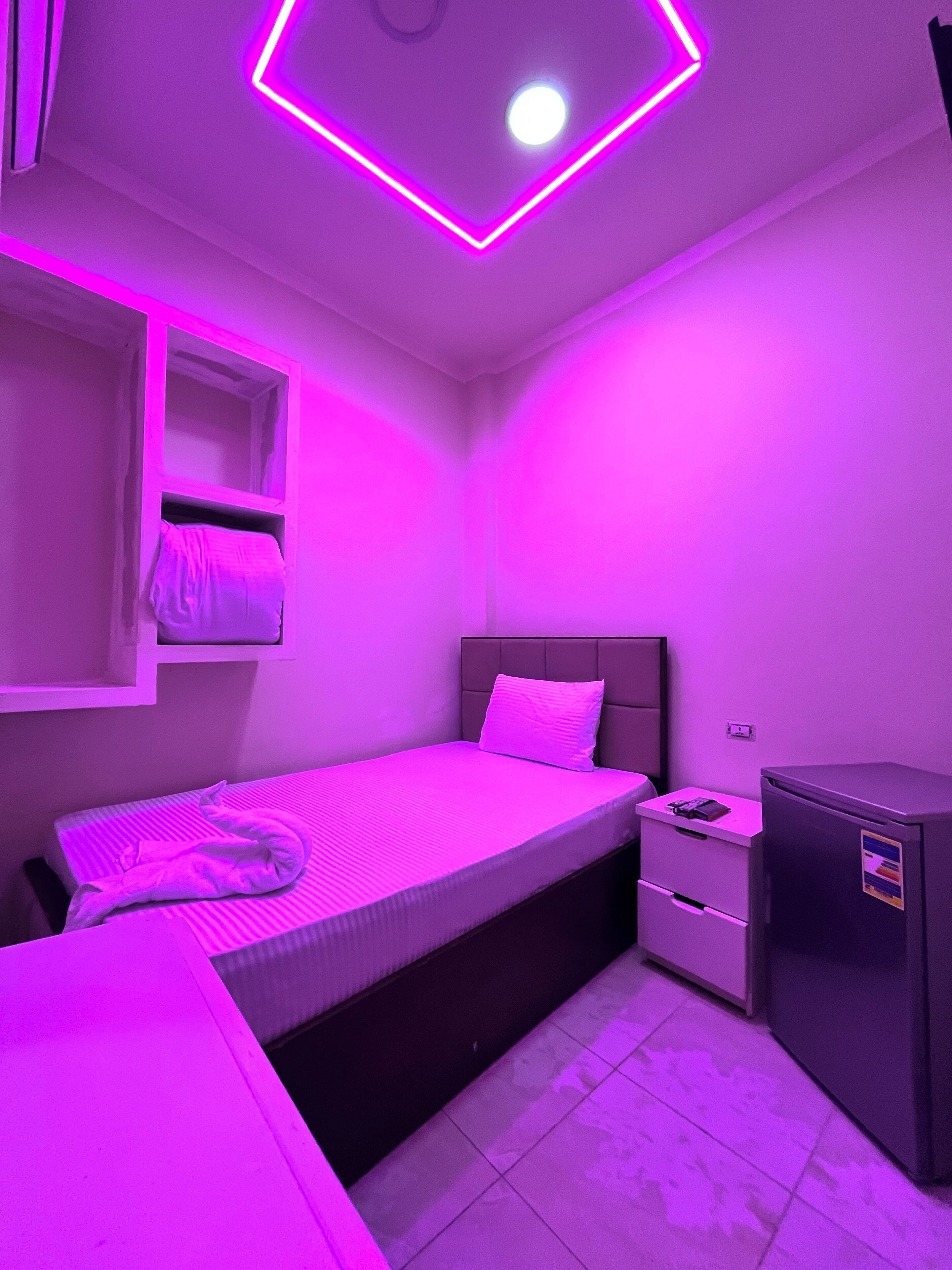 Ein kleines, modernes Schlafzimmer mit Bett, Nachttisch und kleinem Kühlschrank.