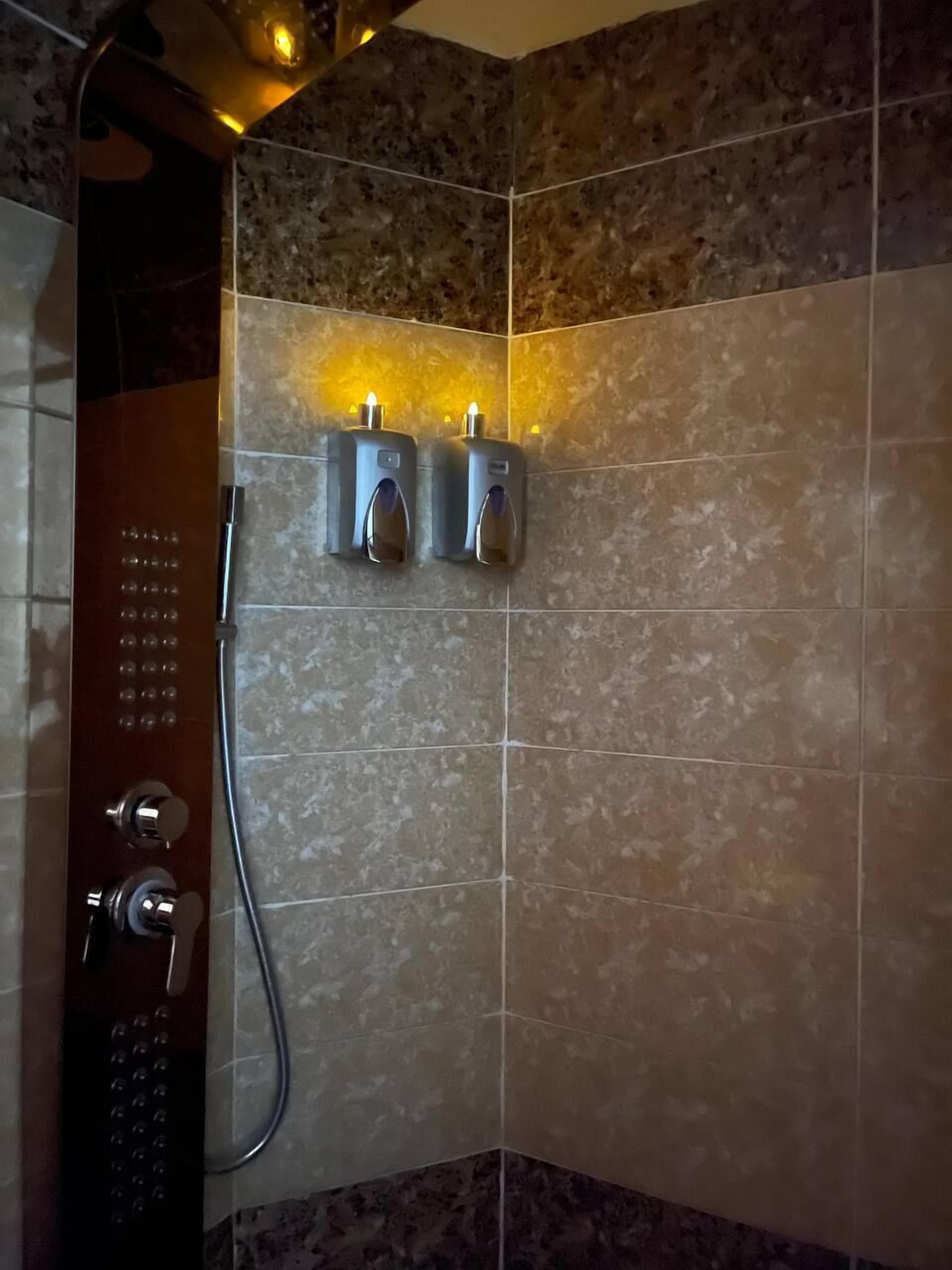 A shower area with a wall-mounted control panel and two illuminated soap dispensers.