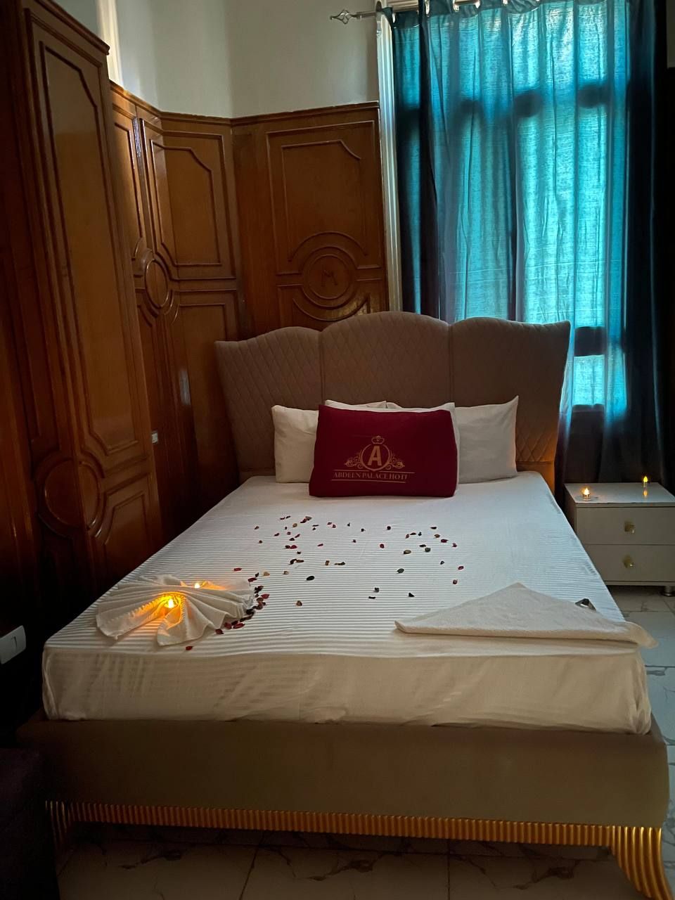 A neatly made bed with a decorative pillow, a bedside table with a lamp, and a window with curtains.