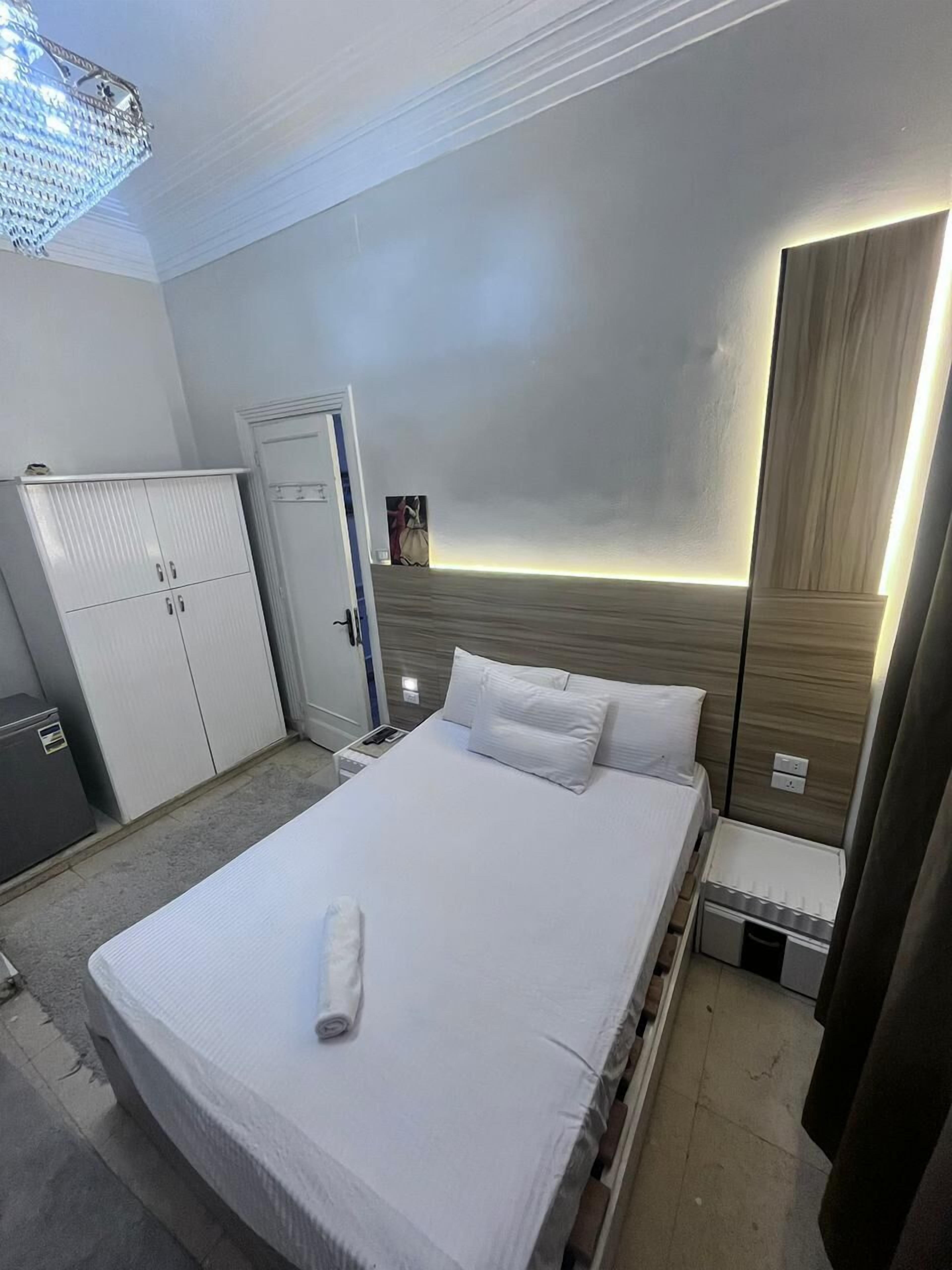 Una habitación de hotel con una cama, un armario, un escritorio y una mesita de noche.