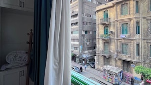 Ein Zimmer mit Blick auf eine Straße, ein Fenster mit Vorhängen und ein hölzerner Hocker.