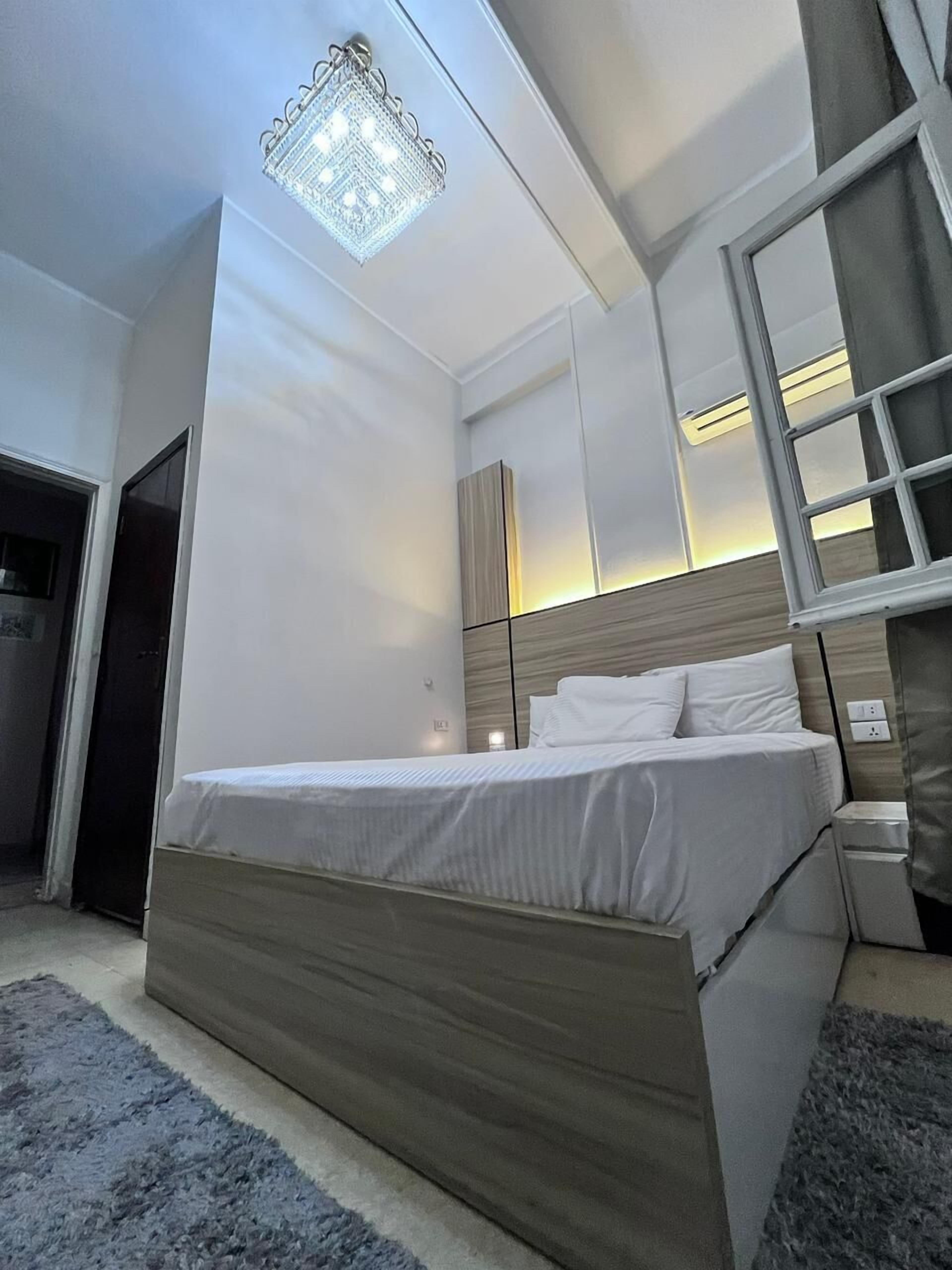Une chambre moderne avec un grand lit, une tête de lit en bois, un miroir et un luminaire fixé au plafond.