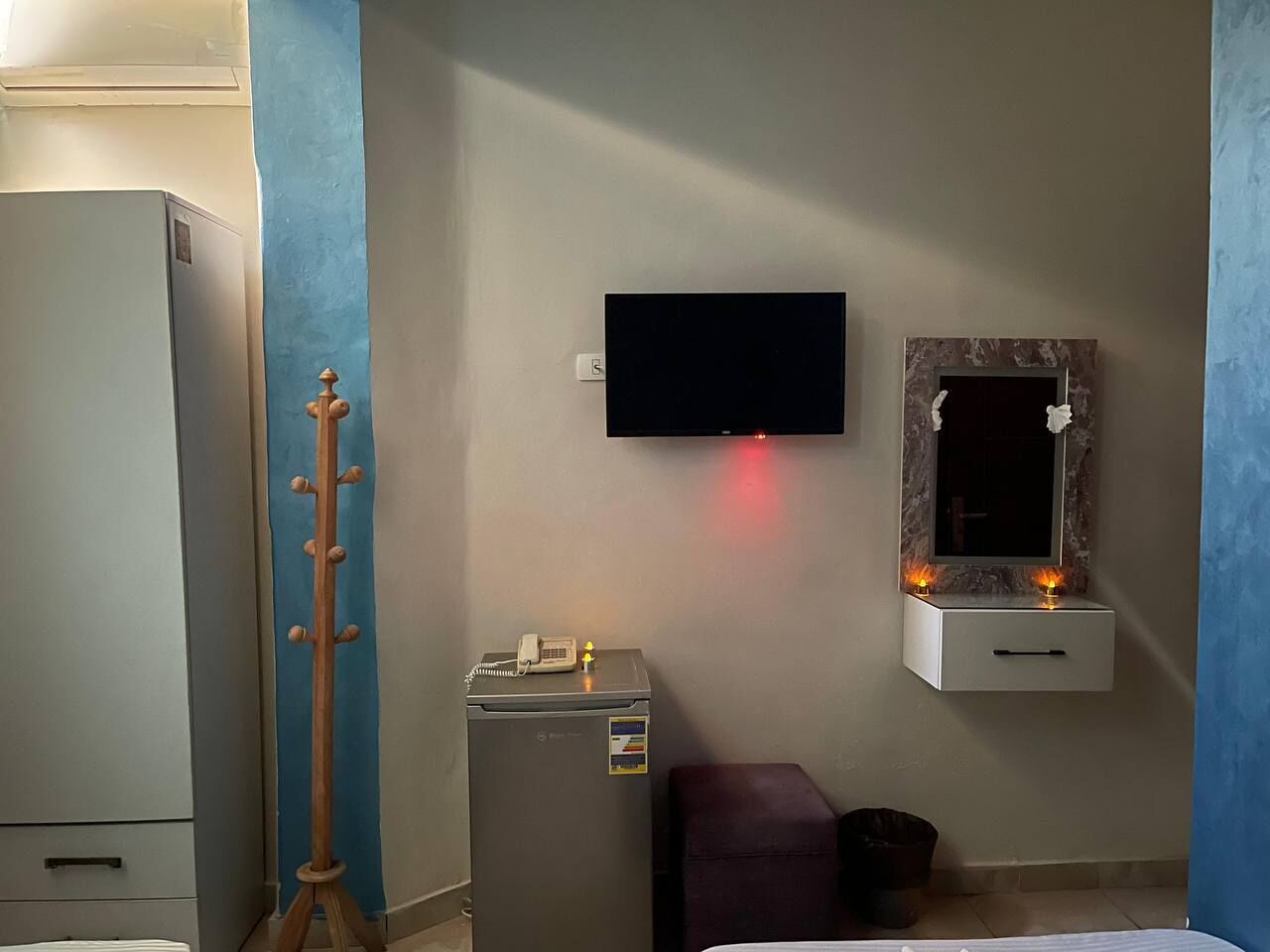 Une chambre dotée d’un téléviseur à écran plat fixé au mur, d’une petite armoire avec un miroir, d’un téléphone et d’un radiateur.