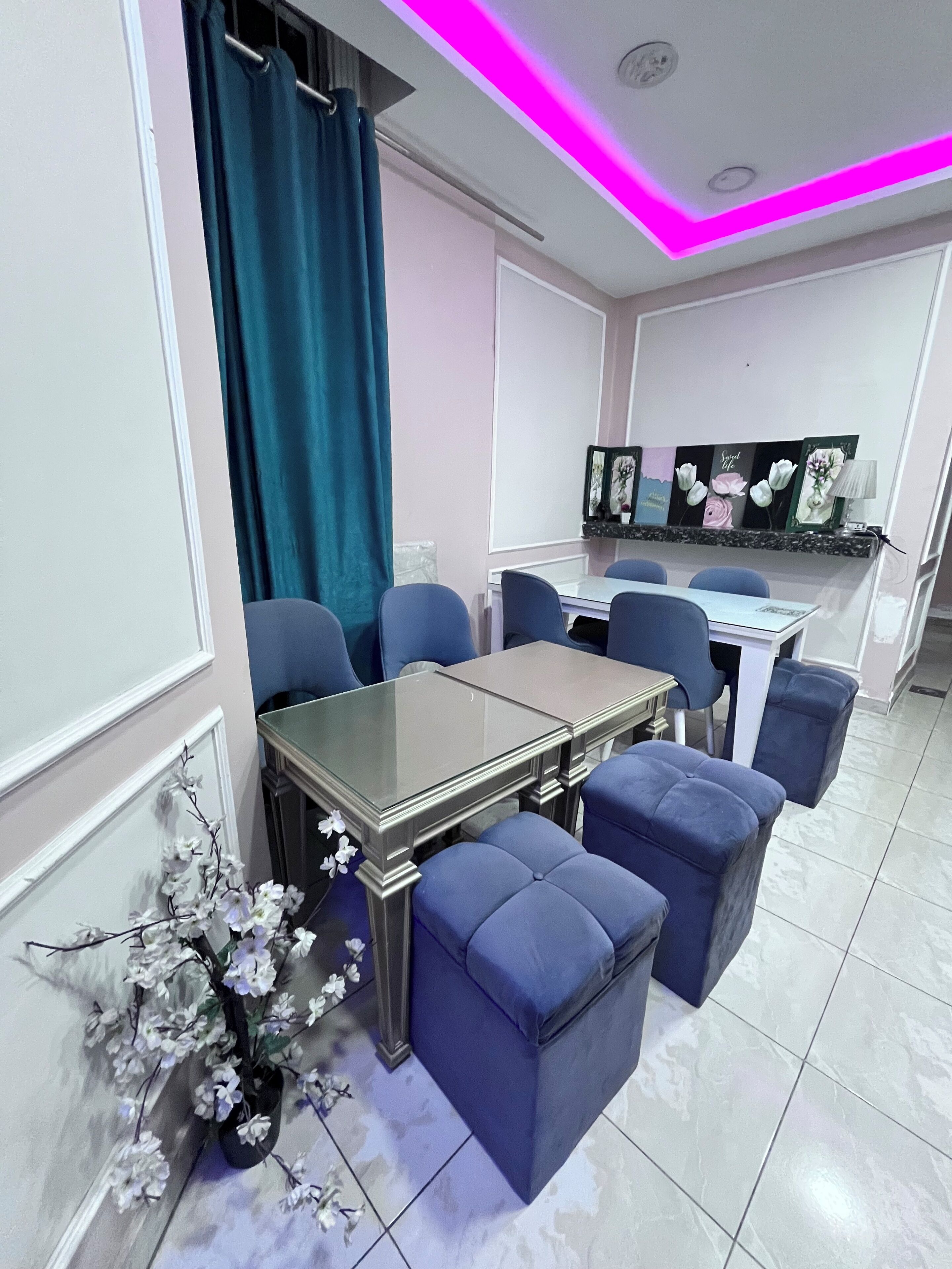 A dining area with a table and chairs, a vase of flowers, and a ceiling with pink lighting.