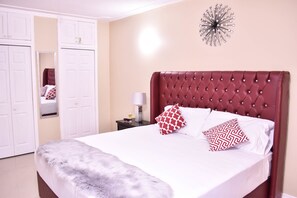 A bedroom with a tufted headboard, white bedding, and patterned pillows.