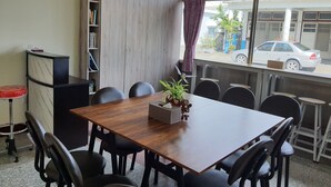 A conference room with a wooden table, black chairs, a bookshelf, and a window with a view of a parked car and buildings outside. - Blackfoot Homestay (Taitung)