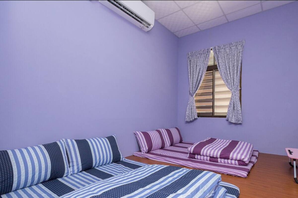 A room with a purple wall, a bed with striped bedding, a sofa with striped pillows, a small table, and a TV mounted on the wall.