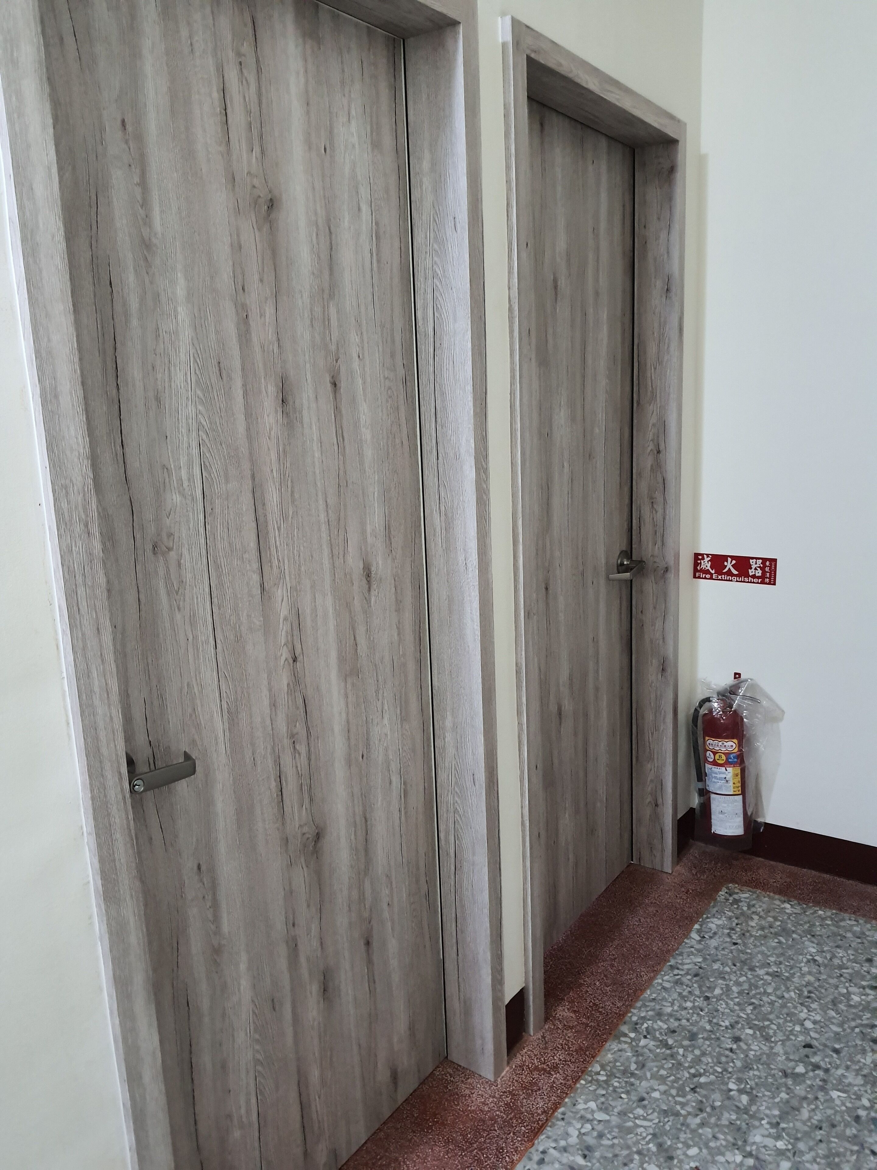 A hallway with wooden doors and a fire extinguisher on the wall.