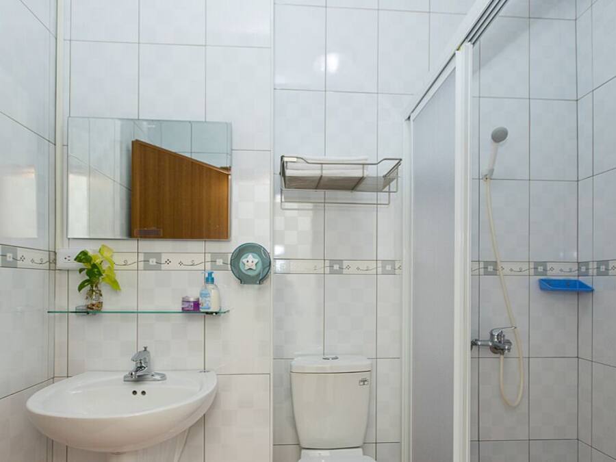 A bathroom with a sink, toilet, and shower. There is a mirror above the sink and a shelf with toiletries.
