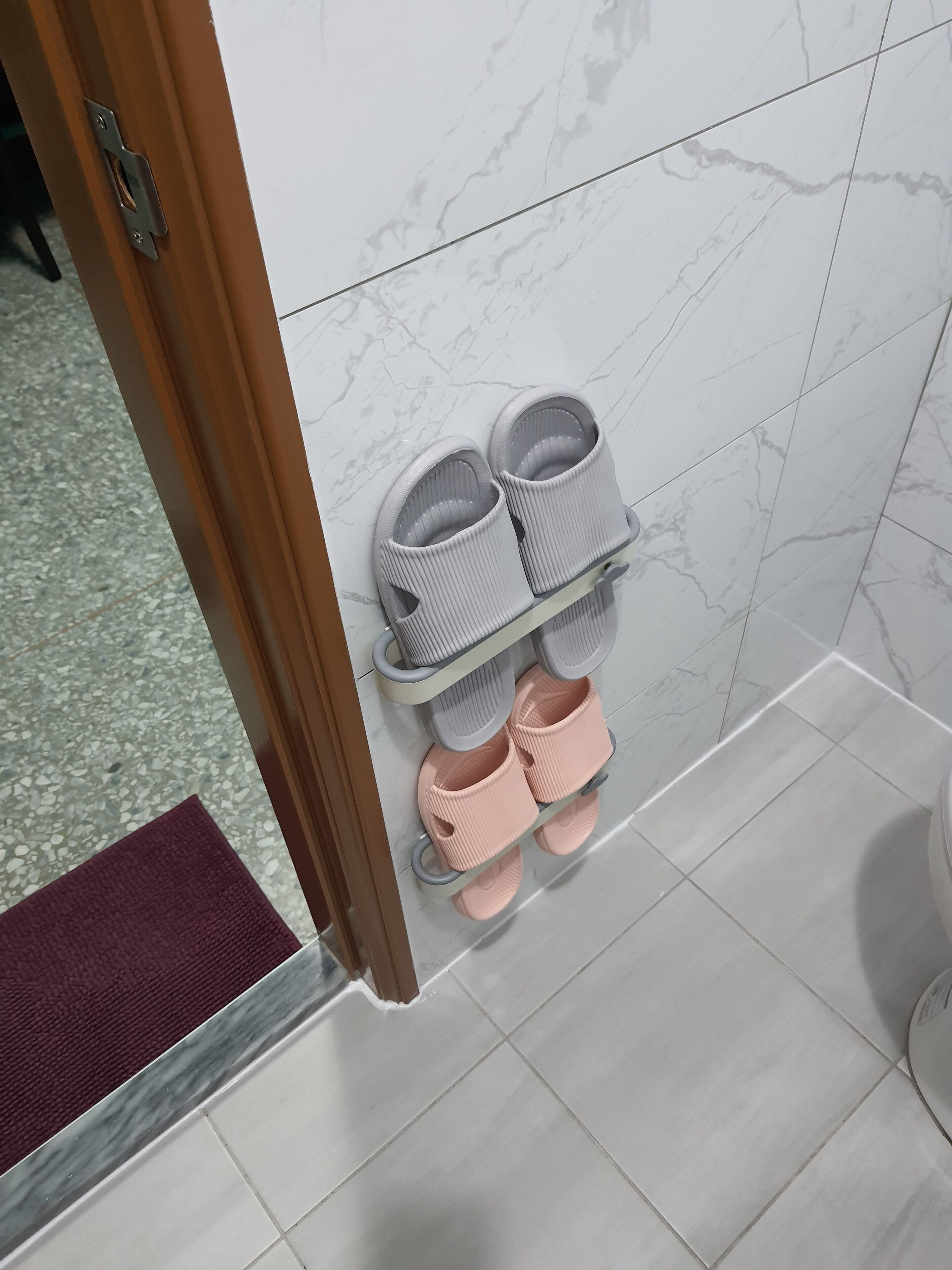 A bathroom with a marble wall, a wooden door, and a shoe rack holding slippers.