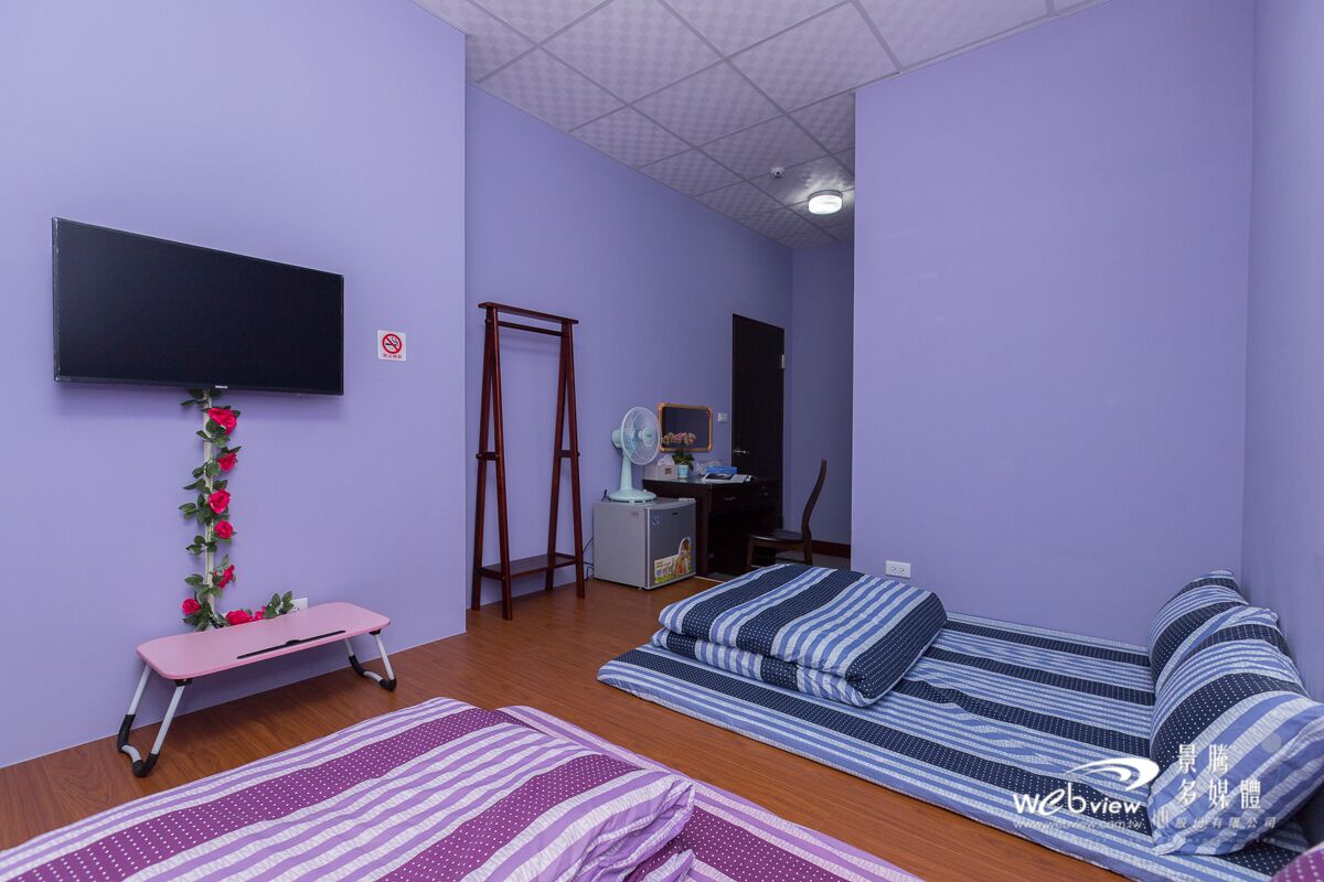 A room with a bed, a desk, a chair, a television, and a small table with a rose decoration.