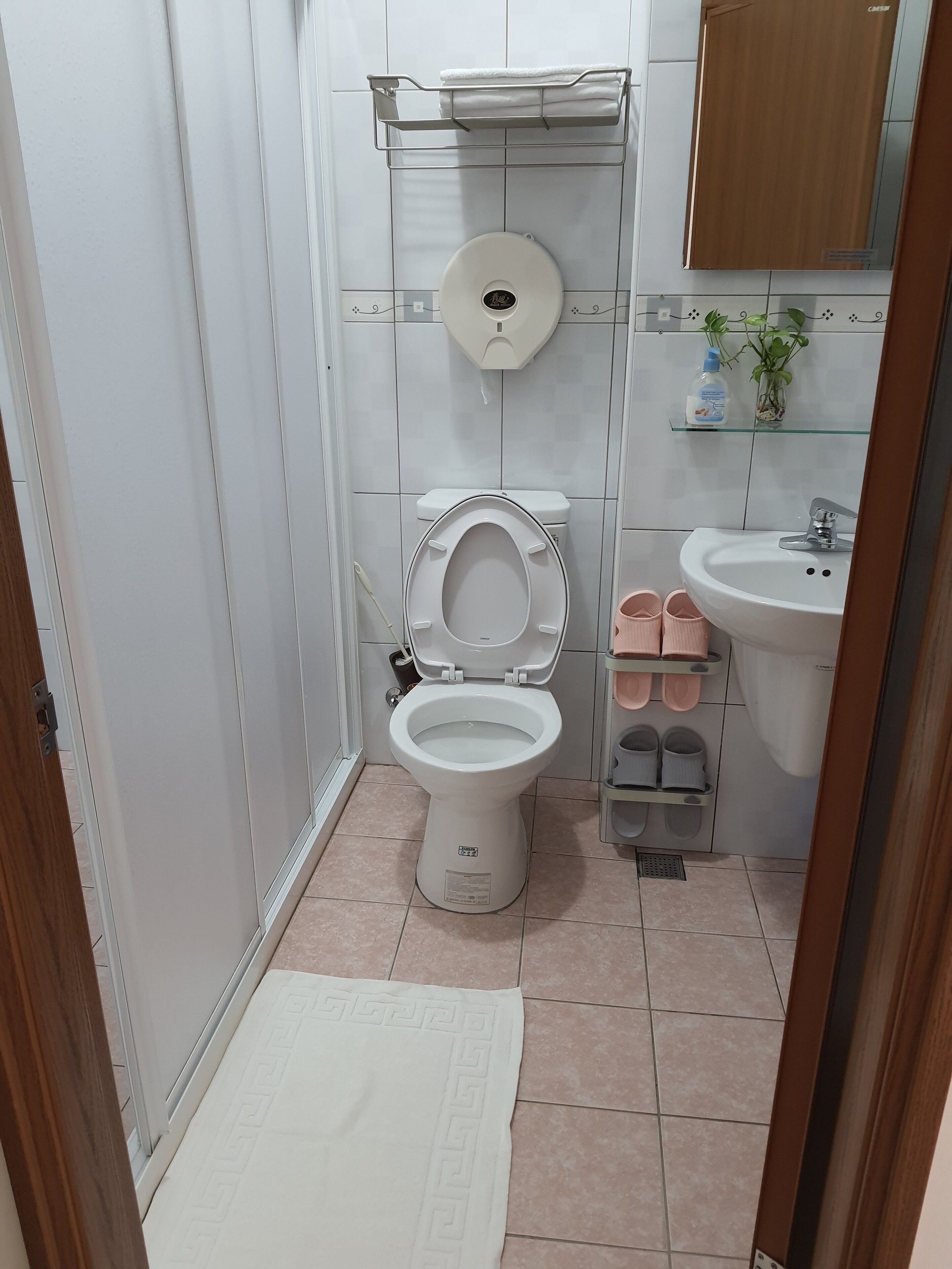 A small bathroom with a toilet, sink, and a shelf with slippers.