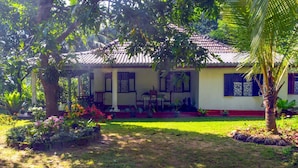 Una casa amb teulada de teules, un porxo amb cadires i un jardí ben cuidat amb plantes i flors diverses.
