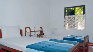 Una habitació amb dos llits, una finestra amb cortina estampada i un capçal de llit de fusta.
