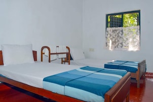 A room with two beds, a window with a patterned curtain, and a wooden headboard.