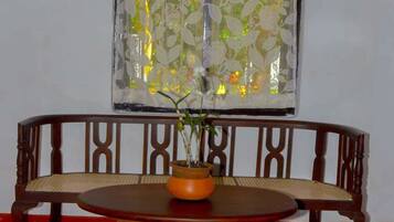 A wooden bench with a woven seat, a round wooden table with a potted plant, and a window with decorative bars and a lace curtain.