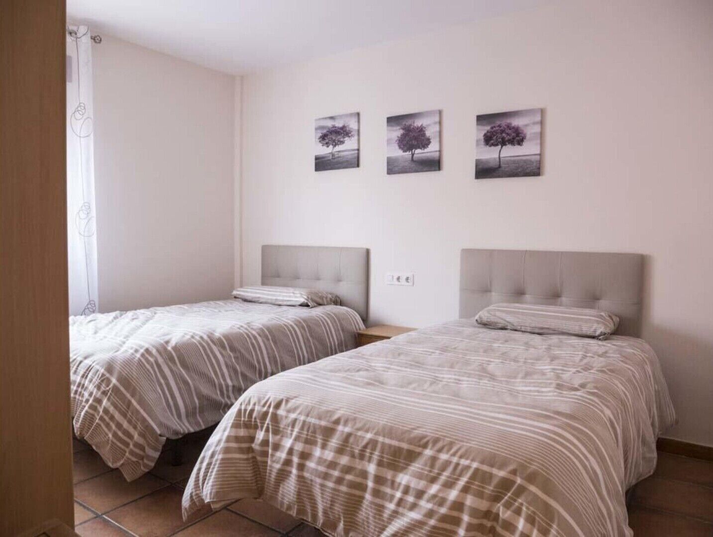 A bedroom with two beds, each with a headboard and a striped bedspread. There are three framed pictures on the wall above the beds.