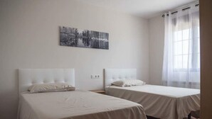 Habitació amb dos llits, una finestra gran amb cortines lleugeres i un quadre de paisatge en blanc i negre a la paret.