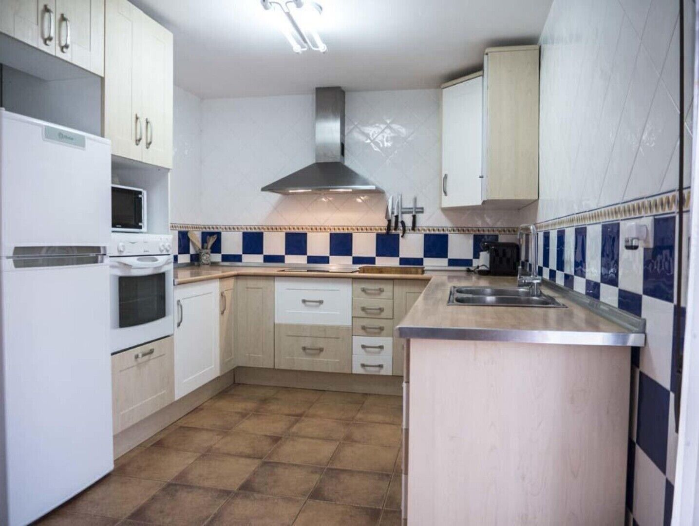A compact kitchen with white cabinets, a stove, microwave, and a stainless steel sink.