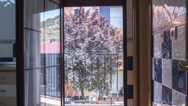 Passadís amb una porta corredissa de vidre que dona a una zona exterior amb un arbre i un edifici al fons.