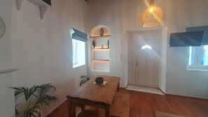 Une pièce avec une table en bois, une plante en pot, une étagère ornée d’objets décoratifs et une porte avec une fenêtre.