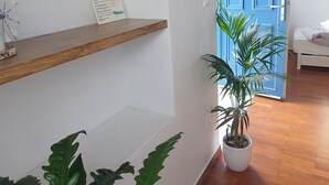 Un couloir avec des étagères en bois, un panneau d’accueil, une porte bleue et des plantes en pot.