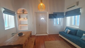 Un salon avec une table en bois, un canapé bleu, un luminaire au plafond et une porte surmontée d’une fenêtre.