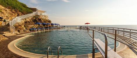 Zona de piscina con solárium de piedra, barandilla metálica y vista al mar.