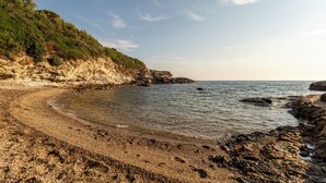 A rocky beach with clear water, a curved shoreline, and a forested cliff. - Four-room apartment in the Capo D'Arco area with direct access to the sea (Rio Marina)