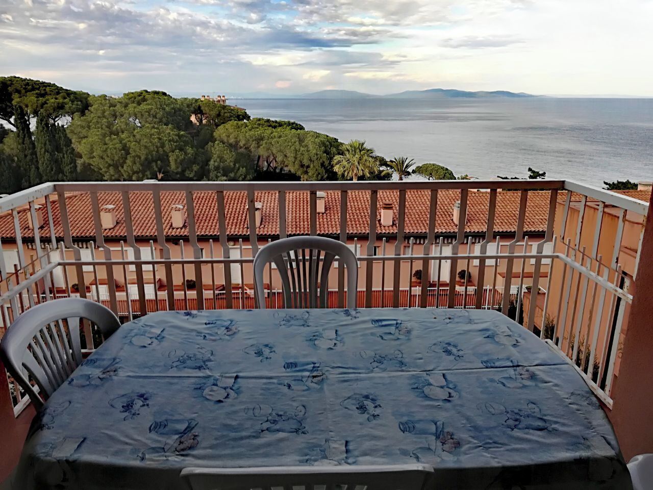 Un balcón con una mesa y sillas, con vistas a un paisaje pintoresco del mar y las colinas.