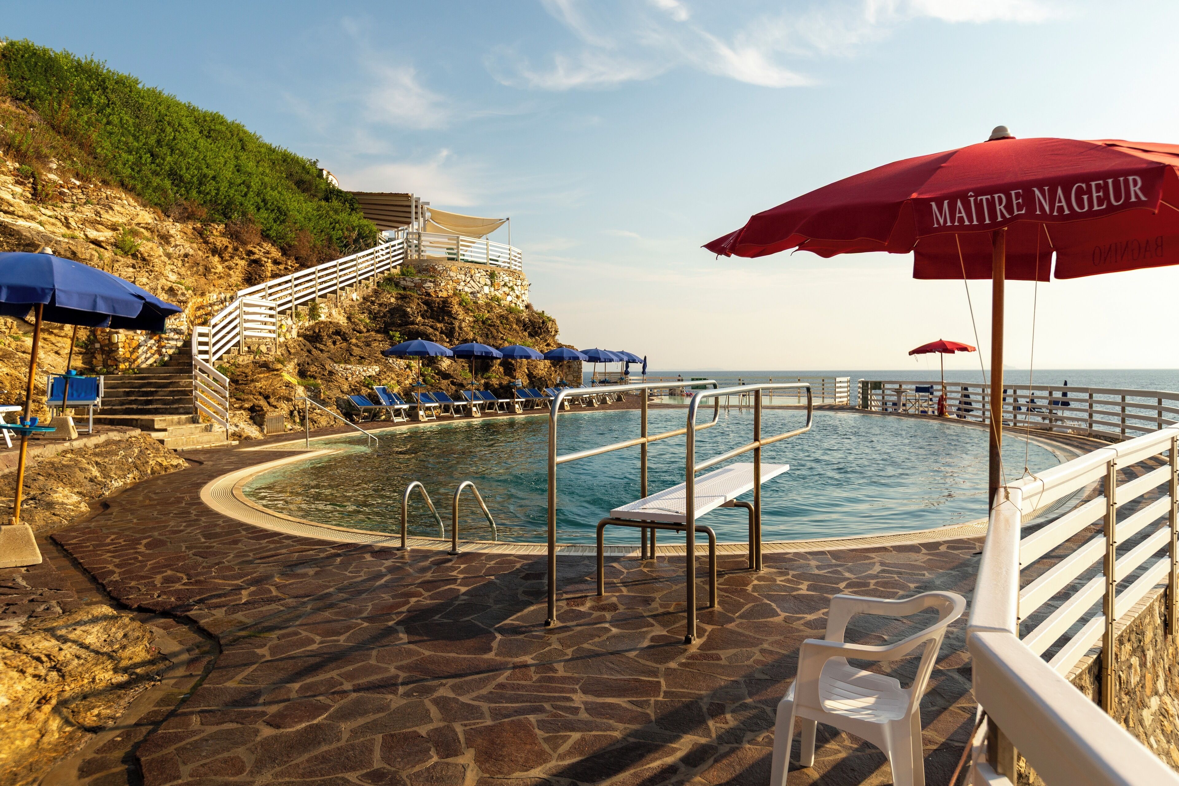 Un espace piscine doté d’un sol en pierre, d’une piscine et d’un escalier menant à une falaise.